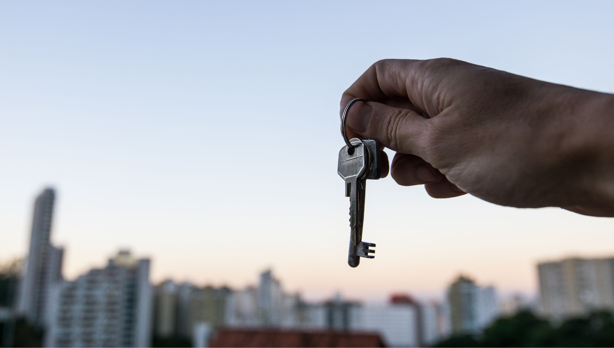 Person holding house keys with a cityscape background, symbolizing a new home purchase or successful mortgage closing at Legend Home Loans.